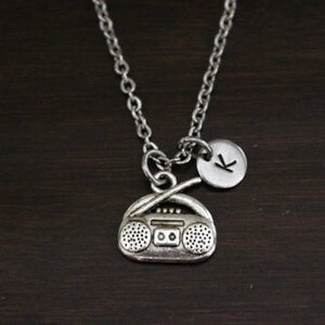 May include: Silver necklace with a charm of a vintage boombox and a small round charm with the letter K.
