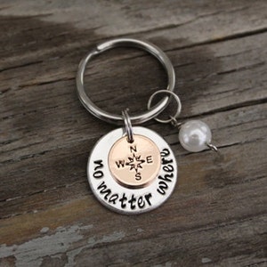 May include: Silver key chain with a compass charm and the words "no matter where" engraved on the charm. A white pearl bead is attached to the key chain.