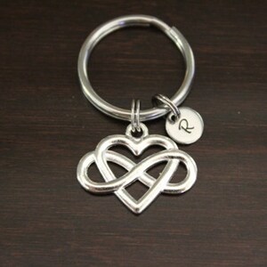 May include: Silver infinity heart keychain with a silver initial charm. The initial charm has the letter "R" engraved on it.