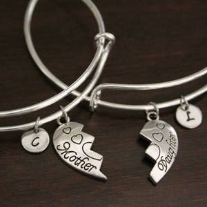 May include: Two silver charm bracelets with heart charms that say "Mother" and "Daughter". The charms are broken hearts that fit together. The bracelets also have initial charms.
