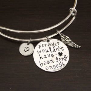 May include: Silver expandable bracelet with three charms. The largest charm is a round disc with the text "Forever wouldn't have been long enough". The other two charms are a small heart and a wing.