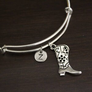 May include: A silver expandable bracelet with a charm of a boot with a black and white pattern and a charm with the letter Z.