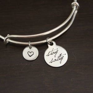 May include: Silver charm bracelet with two charms. One charm has a heart design and the other charm has the text "stay salty".
