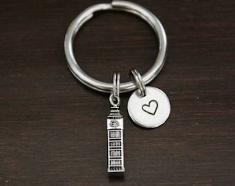 May include: Silver keychain with a charm of Big Ben and a heart charm. The keychain is on a dark wood surface.