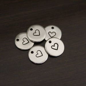 Puede incluir: Cinco dijes de metal plateado con un peque&ntilde;o dise&ntilde;o de coraz&oacute;n. Cada dije tiene un agujero para sujetarlo a un collar o pulsera.