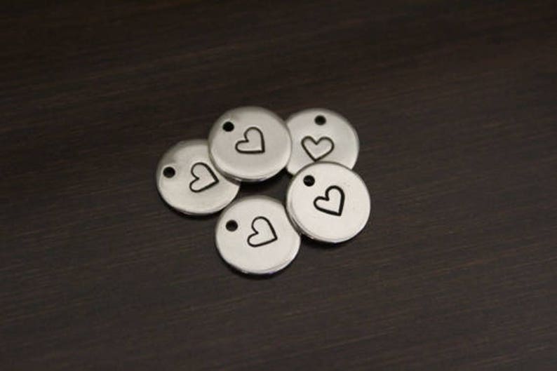 Puede incluir: Cinco dijes de metal plateado con un peque&ntilde;o dise&ntilde;o de coraz&oacute;n. Cada dije tiene un agujero para sujetarlo a un collar o pulsera.