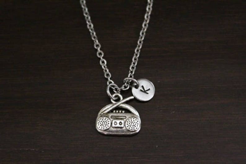May include: Silver necklace with a charm of a vintage boombox and a small round charm with the letter K.