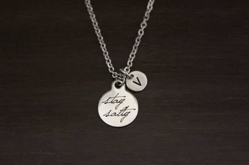May include: Silver necklace with a round pendant that says "Stay Salty" and a smaller round pendant with the letter "V" on it.