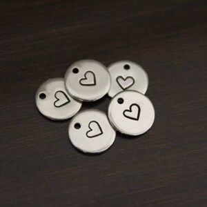 May include: Five silver metal charms with a small heart design. Each charm has a hole for attaching to a necklace or bracelet.