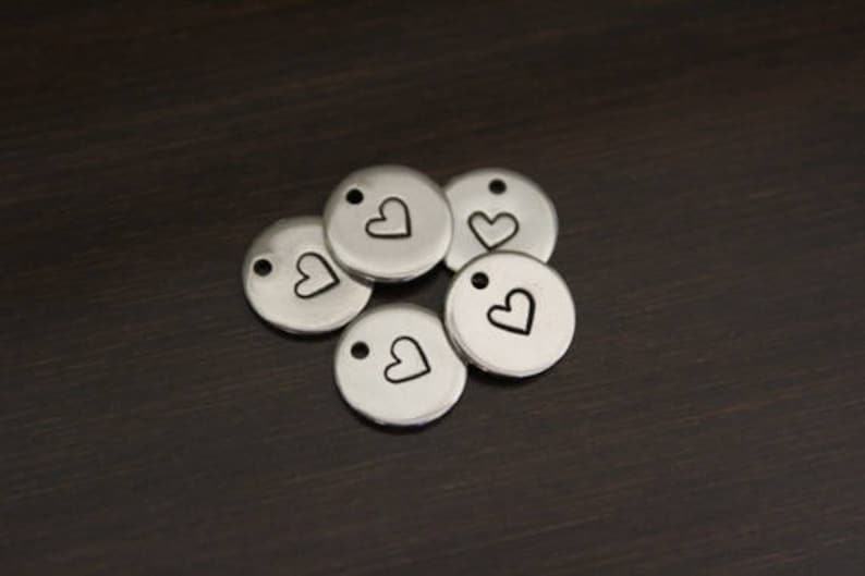 May include: Five silver metal charms with a small heart design. Each charm has a hole for attaching to a necklace or bracelet.