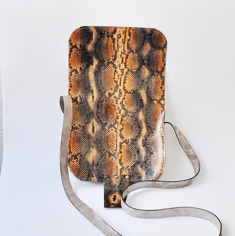 Peut inclure: Un sac &agrave; bandouli&egrave;re en cuir de serpent brun et noir avec une longue bandouli&egrave;re gris clair.