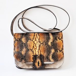 Può includere: Una piccola borsa a tracolla in pelle di serpente con una tracolla bianca e una chiusura a lembo. La borsa ha un motivo in pelle di serpente marrone e nero.
