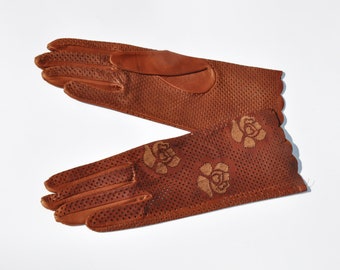 May include: A pair of brown leather gloves with a scalloped edge and a floral design. The gloves are perforated with small holes.