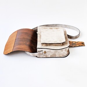 Peut inclure: Un sac &agrave; bandouli&egrave;re en cuir blanc avec un rabat en cuir marron et une bandouli&egrave;re en peau de serpent. Le sac a une poche avant et une fermeture &agrave; glissi&egrave;re.