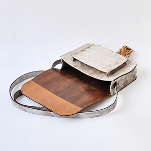 Peut inclure: Un sac &agrave; bandouli&egrave;re en cuir blanc avec une doublure en cuir marron et un rabat en peau de serpent. Le sac a une longue bandouli&egrave;re et une petite poche sur le devant.