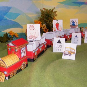 Puede incluir: Un tren de juguete rojo con un vagón amarillo y un gato blanco en la parte delantera. El tren está hecho de cartón y tiene una variedad de otras tarjetas adjuntas, incluyendo un pimiento rojo, un perro, una lata de hojalata y una cola que mueve.