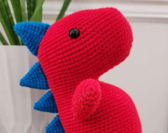 May include: A red crocheted dinosaur toy with blue spikes and black eyes.