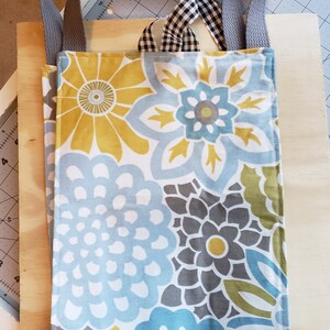 May include: A gray fabric tote bag with blue, yellow, and gray floral print. The bag has two gray fabric straps.