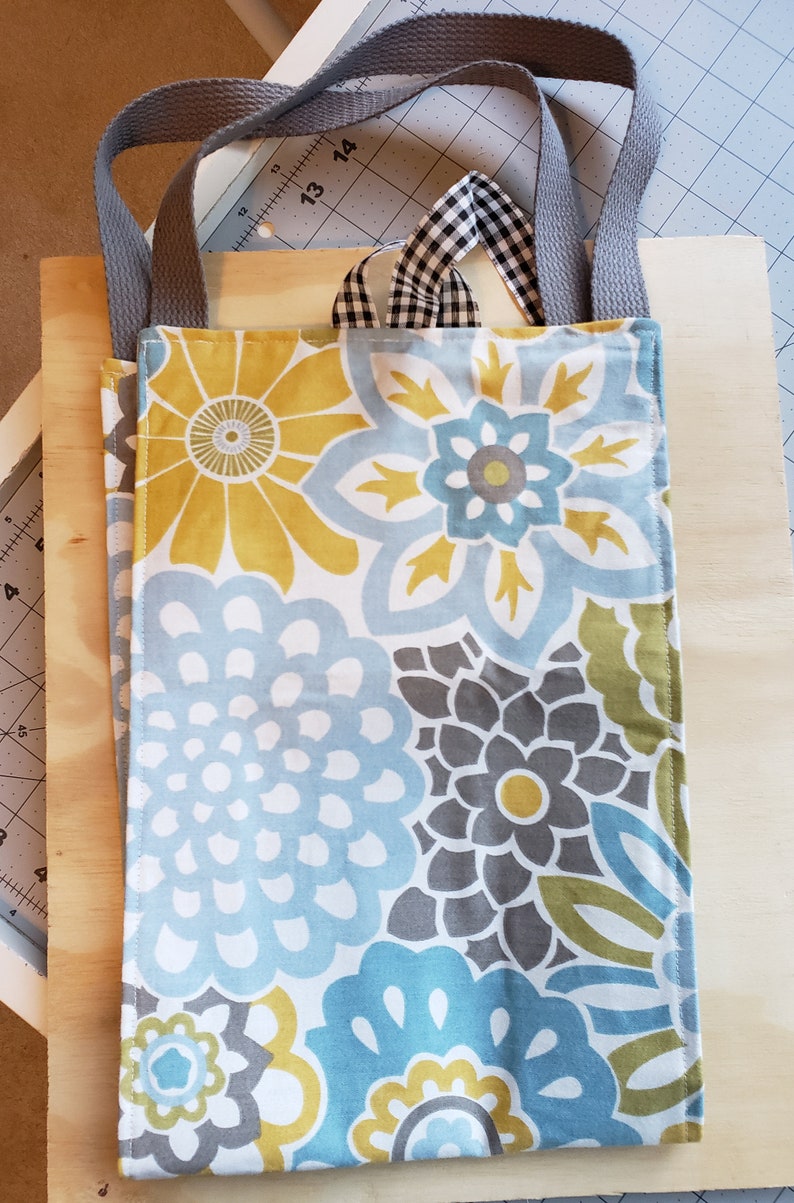 May include: A gray fabric tote bag with blue, yellow, and gray floral print. The bag has two gray fabric straps.