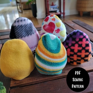 Puede incluir: Cinco juguetes de felpa con forma de huevo de diferentes colores y patrones. Los juguetes están dispuestos en círculo sobre una superficie de madera. El texto "PDF SEWING PATTERN" es visible en la esquina inferior derecha de la imagen.