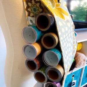 May include: A yellow, green, and blue floral fabric tote bag with a strap. The bag is filled with rolls of wrapping paper, some with labels that say "221002203" and "1958100255".