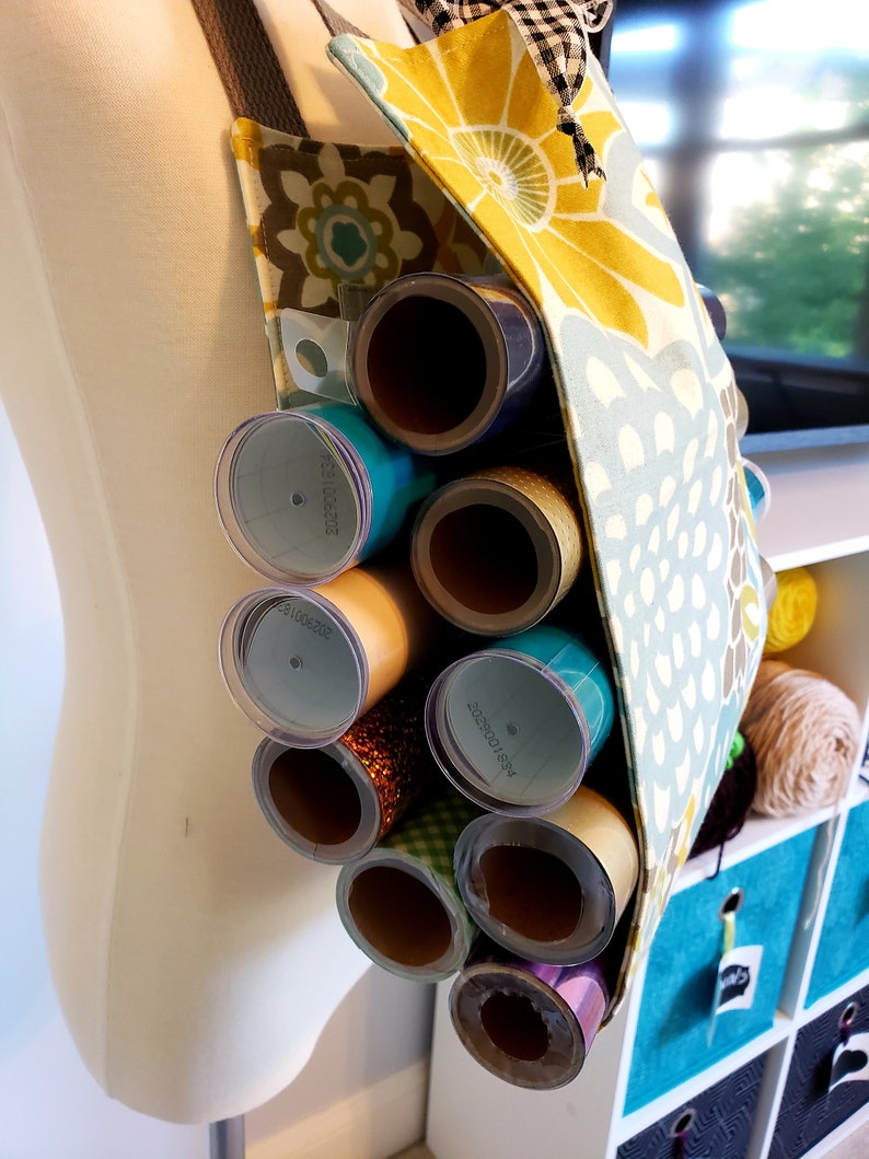 May include: A yellow, green, and blue floral fabric tote bag with a strap. The bag is filled with rolls of wrapping paper, some with labels that say "221002203" and "1958100255".