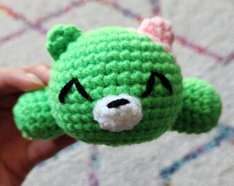 May include: Green crocheted stuffed animal bear with a white face and pink flower on its head.
