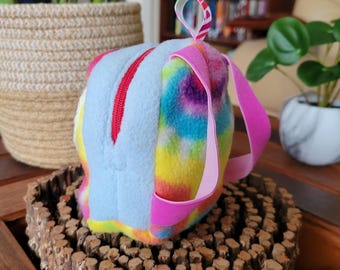 May include: A small, blue and rainbow tie-dye fleece backpack with pink straps. The backpack has a zipper closure and a small loop on the top.