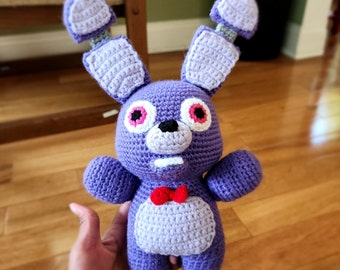 May include: Purple crocheted stuffed toy resembling a rabbit with large ears, red eyes, and a red bow tie.