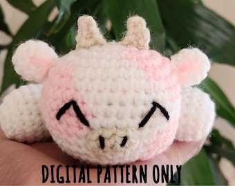 May include: A handmade crochet cow plushie in white and pink. The cow has black embroidered eyes and a smiling mouth. The text "DIGITAL PATTERN ONLY" is at the bottom of the image. The plushie has small horns and ears.