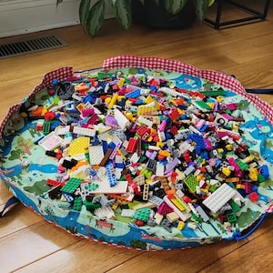 May include: A colorful play mat with a red and white gingham trim, filled with a large collection of colorful plastic building blocks.