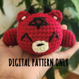 May include: Red crocheted amigurumi toy with horns, a pentagram, and a white face. The toy is being held in a hand. The text "DIGITAL PATTERN ONLY" is visible below the toy.