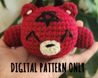 May include: Red crocheted amigurumi toy with horns, a pentagram, and a white face. The toy is being held in a hand. The text "DIGITAL PATTERN ONLY" is visible below the toy.