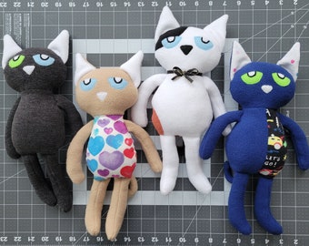 May include: Four plush cat toys with different colors and patterns. The first cat is black with green eyes, the second is tan with a pink and purple heart pattern, the third is white with black spots and blue eyes, and the fourth is blue with green eyes and a yellow and black pattern. The blue cat has the text "Let's Go!" on its belly.