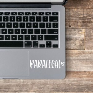 May include: A silver laptop computer with a white sticker on the trackpad that says "PARALEGAL" with a heart symbol.