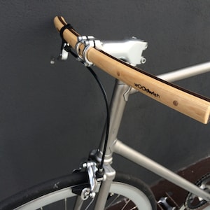 Op de afbeelding: Een zilveren fiets met een houten stuur. Het stuur is gemaakt van bamboe en heeft de tekst "WOODwish" erop gegraveerd.