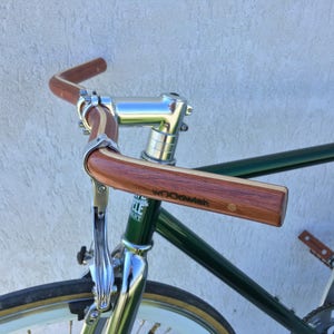 Può includere: Una bicicletta verde con un manubrio in legno e una leva del freno cromata. Il manubrio è etichettato "woodwish".