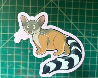 May include: A sticker featuring a cartoon animal with a gray head, tan body, and a black and white striped tail. The sticker has a pink outline and is set against a green grid background. The animal has large ears and a friendly expression.