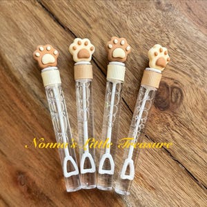 May include: Four clear plastic bubble wands with brown paw print toppers. The wands have a white plastic handle and a white plastic bubble wand attached to the bottom.