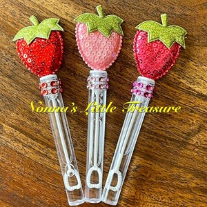 May include: Three clear plastic bubble wands with a strawberry-shaped topper. The toppers are made of red, pink, and light pink sequins with green glitter leaves. Each wand has a clear plastic tube with a small loop at the bottom and a clear plastic handle.