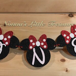 May include: A black and red glitter banner with the word "ONE" in white letters. The banner is decorated with red and white polka dot bows and Mickey Mouse ears. The text "Nonna's Little Treasure" is visible above the banner.