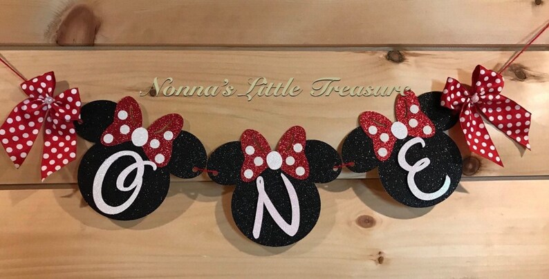 May include: A black and red glitter banner with the word "ONE" in white letters. The banner is decorated with red and white polka dot bows and Mickey Mouse ears. The text "Nonna's Little Treasure" is visible above the banner.