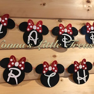 May include: A festive banner with black mouse head shapes, each featuring a white letter spelling "HAPPY BIRTHDAY". Red glitter bows with white polka dots adorn each head. The banner is strung on a red cord.