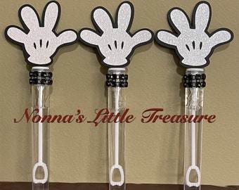 Könnte beinhalten: Drei transparente Seifenblasenstäbe mit weißen, glitzernden Mickey Mouse-Handaufsätzen. Jeder Stab hat ein schwarz-weißes Zierband in der Nähe der Oberseite. Der Text "Nonna's Little Treasure" ist in roter Schreibschrift gedruckt.