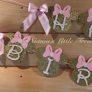 May include: Gold glitter Minnie Mouse ears with pink bows and white centres, spelling out "Happy Birthday" with white letters.