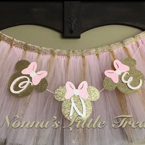 May include: Pink and gold tulle tutu with a banner that says "One" in white letters with pink and gold Minnie Mouse ears.