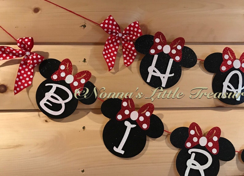 May include: A festive banner with black Mickey Mouse head cutouts spelling out "BIRTHDAY" in white letters. Each cutout has a red bow with white polka dots. The banner is strung on a red string, perfect for a birthday party.