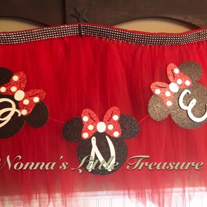 May include: Red tulle skirt with a decorative banner featuring black Mickey Mouse head shapes with white letters and red polka dot bows. The banner is strung across the top of the skirt.