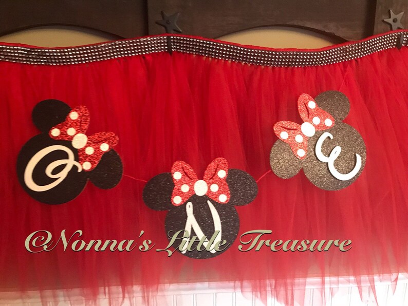 May include: Red tulle skirt with a decorative banner featuring black Mickey Mouse head shapes with white letters and red polka dot bows. The banner is strung across the top of the skirt.