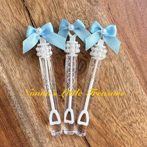 May include: Three clear plastic bubble wands with blue bows and pearl accents. The wands are filled with bubble solution and have a small plastic wand at the end.